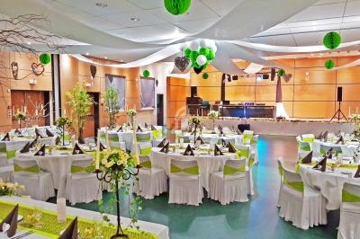 Salle de réception décorée avec des tables dressées, des chaises ornées de nœuds verts et des suspensions décoratives.