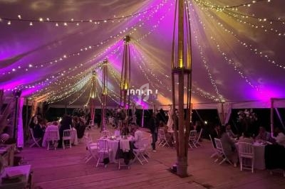 Intérieur d'une tente éclairée par des guirlandes lumineuses et des projecteurs colorés, avec des tables dressées et des…