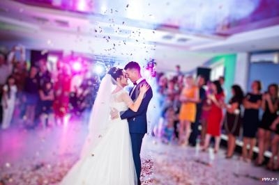 Un couple de mariés danse au centre d'une salle festive, entouré d'invités et de confettis colorés.