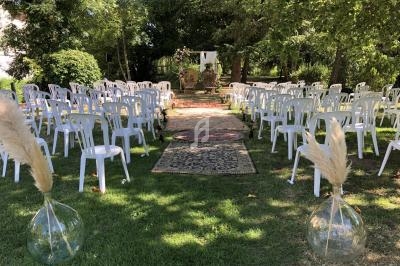 Chaises blanches disposées en rangées de chaque côté d'une allée ornée de tapis, dans un jardin verdoyant.