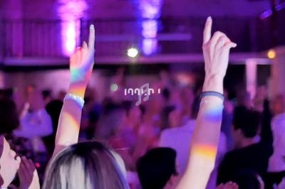 Personnes dansant dans une salle éclairée par des lumières colorées, avec des bras levés au premier plan.