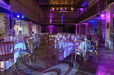 Salle de réception décorée avec des tables rondes dressées, éclairage violet et murs en pierre apparente.