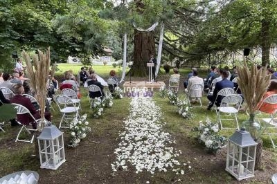 Cérémonie de mariage en plein air avec des invités assis, allée décorée de pétales de fleurs et grand arbre en arrière-plan.