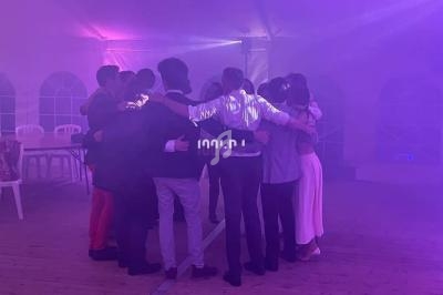 Un groupe de personnes se tient en cercle, bras dessus bras dessous, dans une salle éclairée par des lumières violettes.