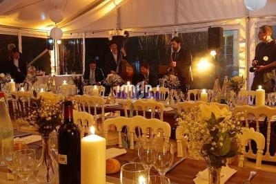 Salle de réception décorée pour un dîner, avec tables dressées, bougies allumées et invités en arrière-plan.