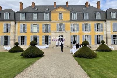 Façade d'un grand bâtiment historique jaune avec des fenêtres grises, entouré de pelouses et d'arbustes taillés.
