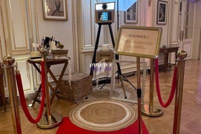 Photobooth avec écran tactile, éclairage studio, tapis rouge et cordons dorés dans un intérieur élégant.