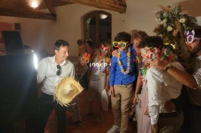 Un groupe de personnes déguisées avec des accessoires colorés pose devant une borne photo dans une salle festive.