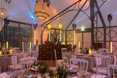 Salle de réception décorée avec des tables dressées, éclairages chaleureux et une piste de danse avec équipement DJ.