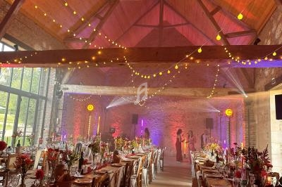 Salle de réception décorée pour un événement, avec guirlandes lumineuses suspendues et tables dressées.