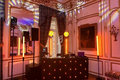 Console de DJ éclairée par des lumières colorées dans une salle ornée de moulures et de rideaux élégants.