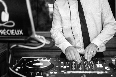 Un DJ en chemise et cravate mixe de la musique sur une table de mixage dans un environnement intérieur.