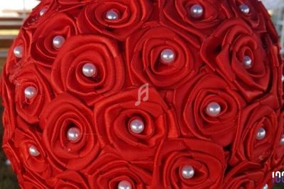 Bouquet sphérique composé de roses en tissu rouge ornées de perles blanches au centre.