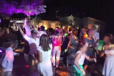 Des personnes dansent et célèbrent en soirée, éclairées par des lumières colorées dans un espace extérieur.