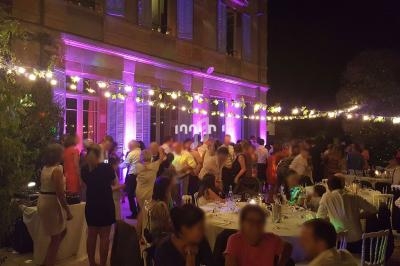 Groupe de personnes dans une réception en soirée, avec guirlandes lumineuses et éclairage coloré sur un bâtiment.