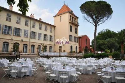 Tables rondes dressées pour un événement en plein air devant un grand bâtiment historique avec un arbre imposant.