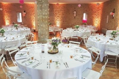 Salle de réception décorée avec des tables rondes dressées, nappes blanches et centres de table floraux.