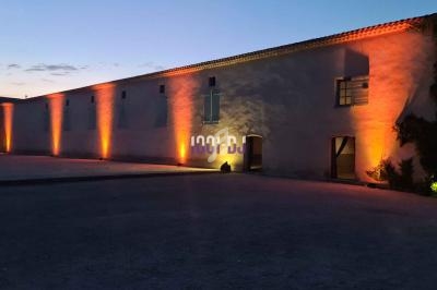 Façade d'un bâtiment éclairée par des lumières orange au crépuscule, avec un ciel partiellement nuageux.