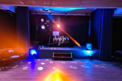 Salle de spectacle avec scène éclairée par des projecteurs colorés et rangées de chaises vides.