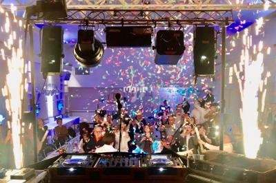 Vue depuis une scène avec des platines DJ, des confettis et une foule en fête dans une salle illuminée.