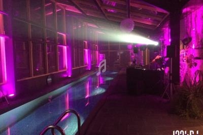 Salle avec piscine éclairée par des lumières violettes, un DJ installé à droite près de son équipement.