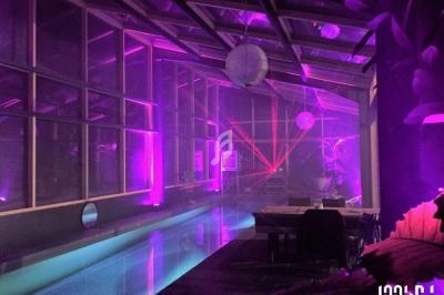 Espace intérieur avec piscine, éclairage violet et rose, décorations suspendues et ambiance tamisée.