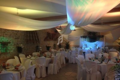 Salle de réception décorée avec des drapés blancs au plafond, tables rondes dressées et chaises couvertes.