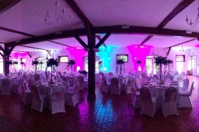 Salle de réception décorée avec des tables rondes, nappes blanches et éclairage coloré rose et bleu.
