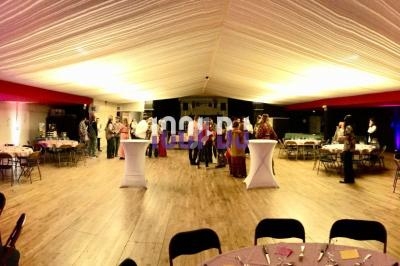 Salle de réception avec tables rondes dressées, éclairage tamisé et invités debout discutant au centre.