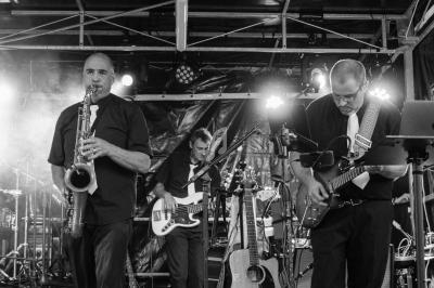 Musiciens jouant sur scène avec des guitares, un saxophone et un éclairage de concert en arrière-plan.