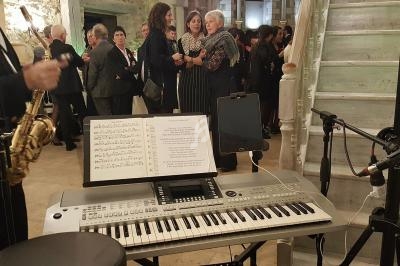 Clavier électronique avec partitions en premier plan, invités discutant dans une salle en arrière-plan.