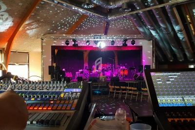 Salle de spectacle avec scène éclairée, instruments de musique et consoles de mixage au premier plan.