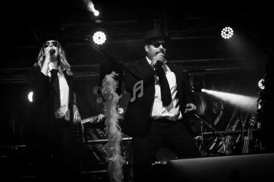 Deux chanteurs en costume sombre et lunettes de soleil se produisent sur scène sous des éclairages de concert.