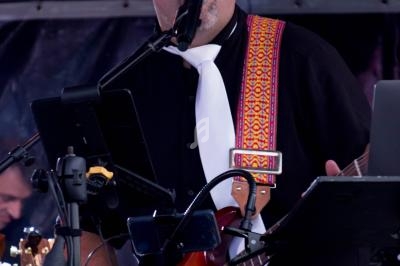 Un musicien chante en jouant de la guitare électrique sur une scène, équipé d'un micro et de supports pour partitions.