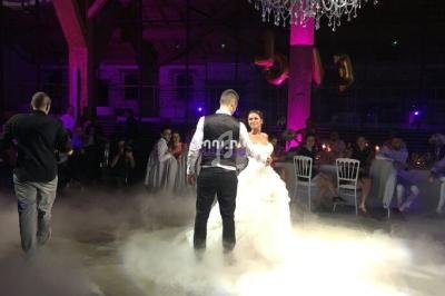 Un couple danse sous un lustre dans une salle éclairée de lumières violettes, entouré d'invités assis.
