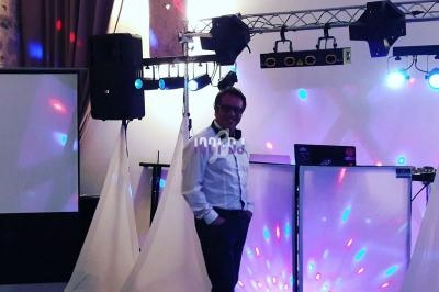 Un DJ souriant debout devant son équipement lumineux dans une salle de réception.