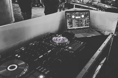 Poste de DJ avec platines et ordinateur portable, en arrière-plan des personnes dans un lieu animé.