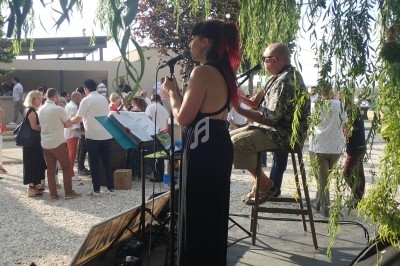 Une chanteuse et un musicien jouent sur une scène en plein air lors d'un événement avec des spectateurs en arrière-plan.