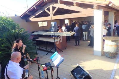 Un duo de musiciens joue en extérieur sous un auvent lors d'un événement avec des invités en arrière-plan.