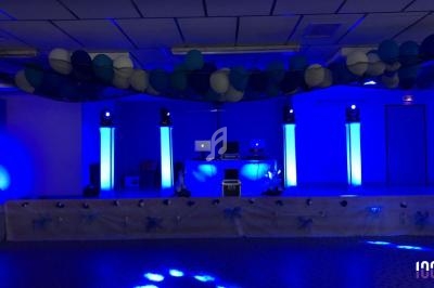 Salle décorée en bleu avec des ballons suspendus, éclairage lumineux et équipement de DJ sur une scène.