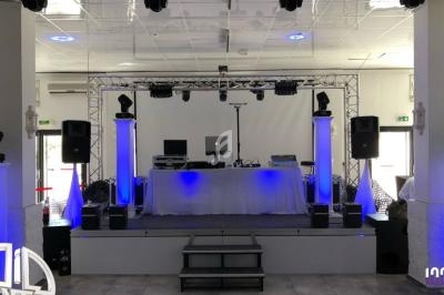 Scène équipée d'une table de mixage, d'enceintes et d'éclairages bleus dans une salle lumineuse.