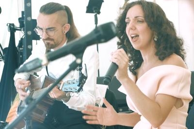 Une femme chante au micro tandis qu'un homme joue de la guitare dans un cadre lumineux.
