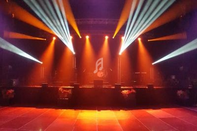 Scène de concert vide éclairée par des projecteurs colorés orange et blancs, avec un sol brillant et des équipements en…