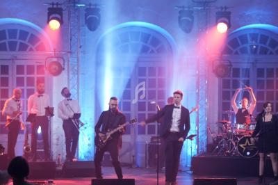 Groupe de musiciens et chanteurs se produisant sur scène dans une salle illuminée de lumières colorées.