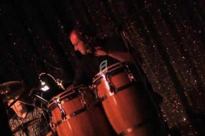 Un musicien joue des congas sur une scène sombre avec un fond scintillant.