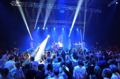Foule dansant devant un groupe de musique sur une scène éclairée par des projecteurs bleus dans une salle de concert.