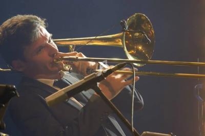 Un musicien joue du trombone sur scène, éclairé par des projecteurs.