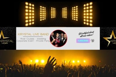 Salle de concert avec public levant les mains, éclairée par des projecteurs dorés et une bannière promotionnelle au centre.