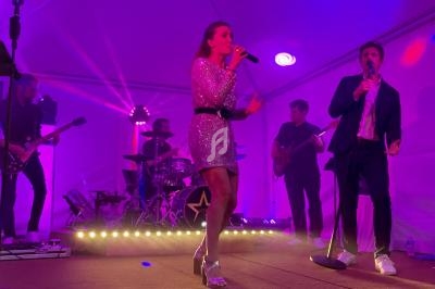 Groupe de musiciens et chanteurs performants sur scène sous un éclairage violet dans une tente.