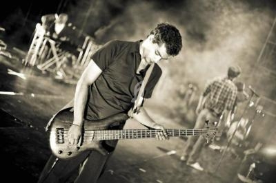 Un musicien joue de la guitare basse sur une scène, éclairée par des projecteurs, avec d'autres artistes en arrière-plan.